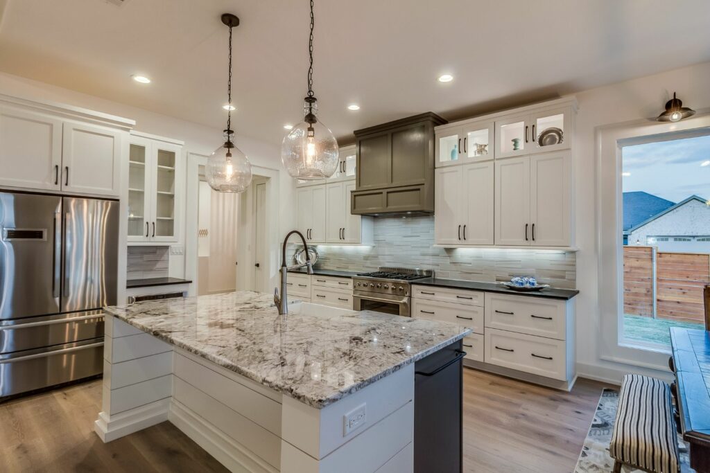Where Style Meets Substance - luxury kitchen with granite countertops, decorative lighting, side-by-side refrigerators, stainless steel appliances and high ceilings